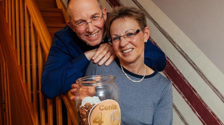 Klaus Matthießen und Ulrike Matthießen stehen auf einer Treppe und halten ein Glas mit Spenden Cents von der Spendenaktion Cents4Children in der Hand